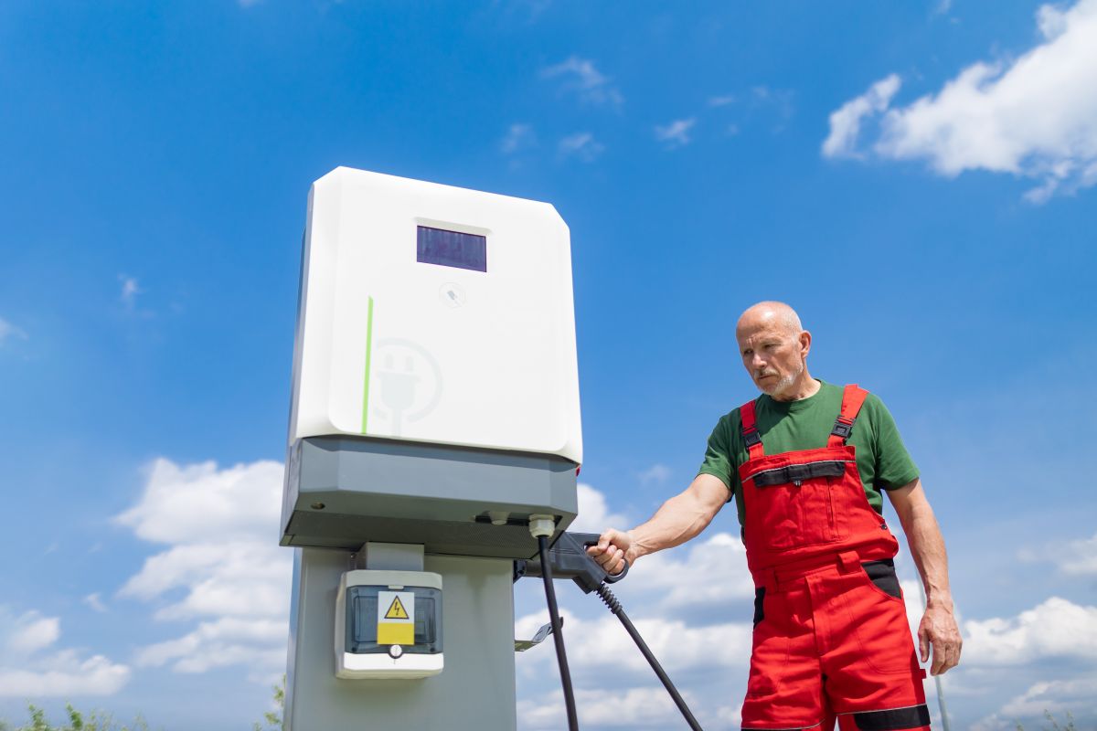 Mężczyzna w czerwonym kombinezonie przy instalacji stacji ładowania samochodów elektrycznych.