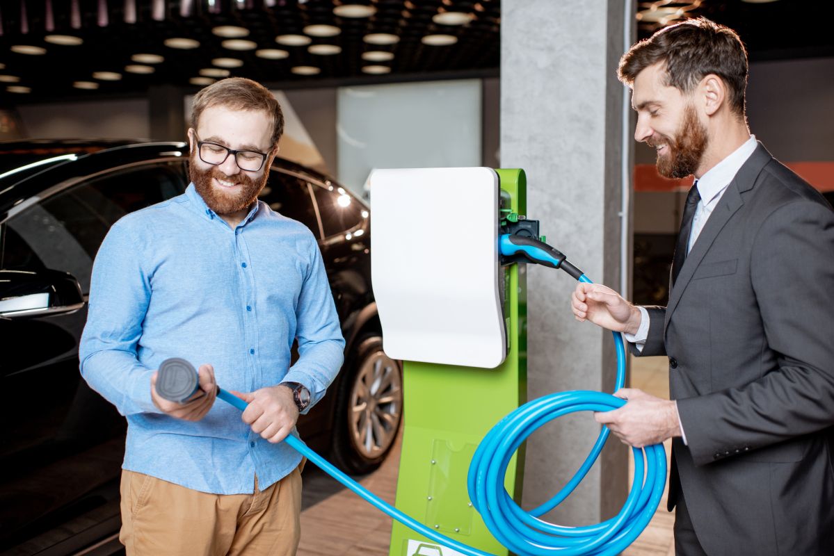 Dwóch mężczyzn przy stanowisku ładowania, oferowanym przez producenta stacji ładowania samochodów elektrycznych.