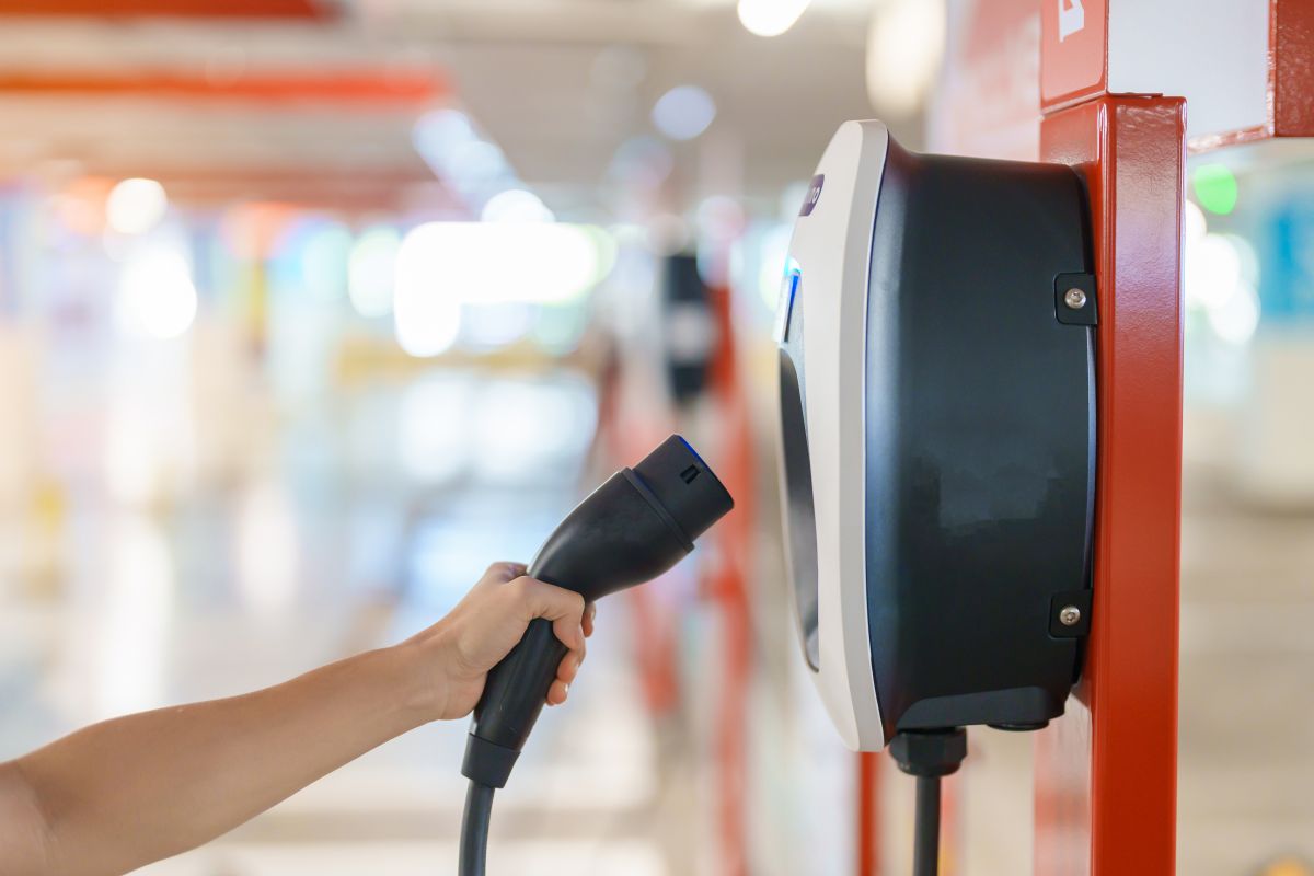 Ręka trzyma wtyczkę do ładowania pojazdów elektrycznych od producenta stacji ładowania samochodów elektrycznych.