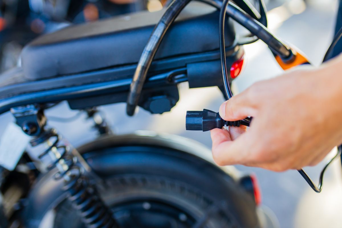 Zdjęcie przedstawia rękę podłączającą przewód do motocykla na stacji ładowania motocykli i skuterów elektrycznych.