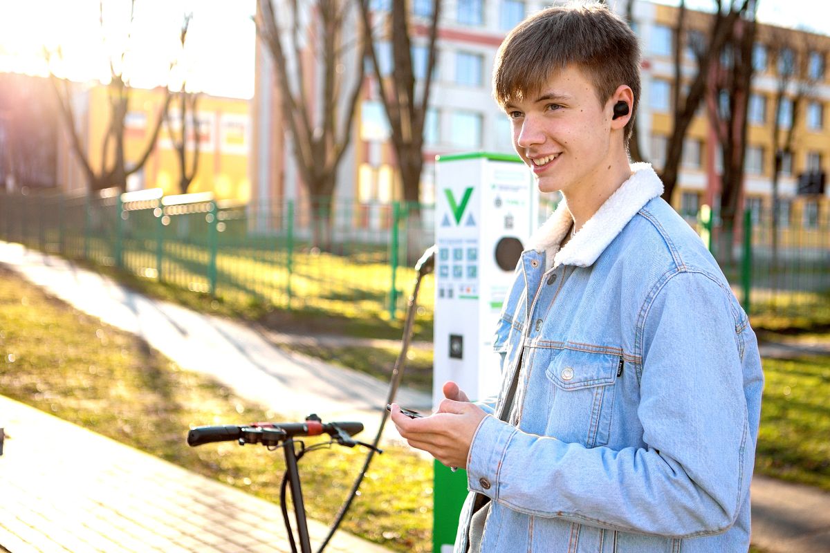 Mężczyzna przy stacji ładowania rowerów elektrycznych i hulajnóg, uśmiecha się, trzymając telefon.